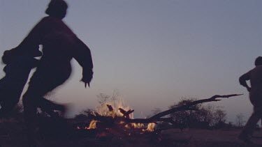 Bushman camp , with campfire a slight pink glow in the sky , dusk with young boys playing around campfire