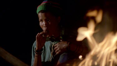 face of bushman woman with baby sitting beside fire , eating warthog steak