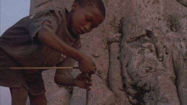 bushmen child fixing his bow and tying string in front of huge baobab tree
