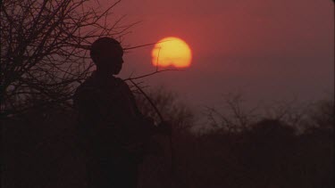 bushman fires arrow from bow against sunset