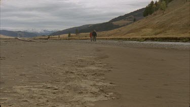MWS people walking toward camera on sandy riverbed with grassy hill surroundings, pan down to coyote track