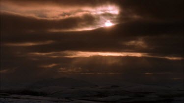 snowy mountains with soft sunlight peeping through the clouds, at sunset