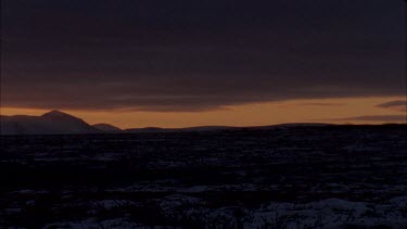 sunset behind snowy mountains, two people walk slowly across the screen in silhouette.