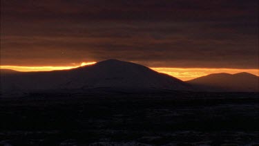 sunset behind snowy mountains, two people walk slowly across the screen in silhouette.