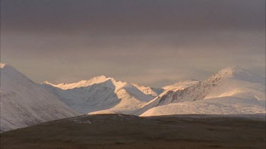 snow capped mountains in tundra landscape, fast moving low cloud