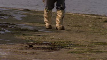 Inuit's boots as he walks toward camera on rocky land at edge of lake