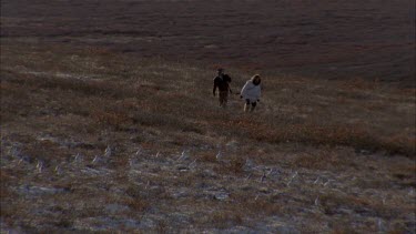 Two Inuit trackers walk through tundra landscape