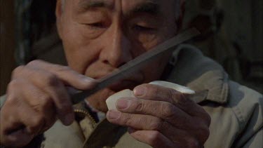 Inuit's head as he carves the ivory sculpture with knife. Pan to CU of man's hands showing sculpting technique
