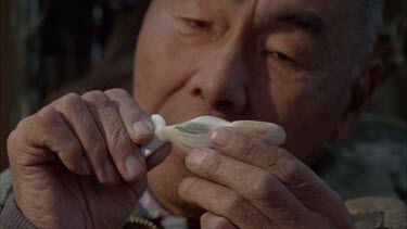 CU of Inuit holding the whale sculpture in his fingers, analyzing edges and smooth surface contours
