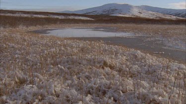 Water in foreground with snow scattered banks, snowy mountain in background