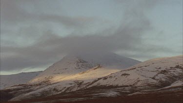 Dark cloud over snow covered mountains, tundra landscape, sun shine onto mountain