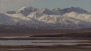 Flat tundra landscape with patches of water and snowy Mt Denali in background