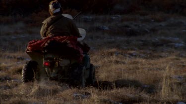 Inuit hunter with gun mounting his buggy car and driving away over rocky tundra landscape