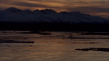 sunset ice flow on river reflecting soft sun rays behind mountains