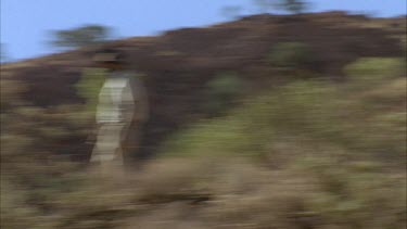man walking across the dry bush landscape down slope.