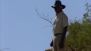 MWS of aboriginal man walking in semi arid landscape up and then down a hill, scenic surrounding