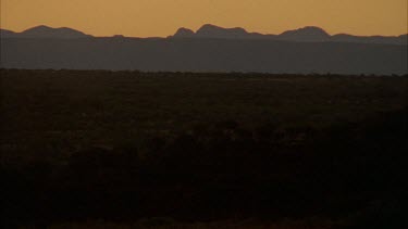 WS scenic shot of the sun setting with its rays peeping over the horizon and blocked by rocky hill in foreground