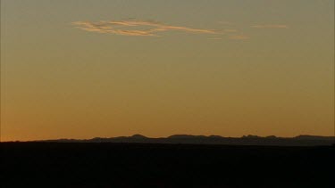WS scenic slow pan of the semi arid plains, orange sky glowing behind blue hills in the distance