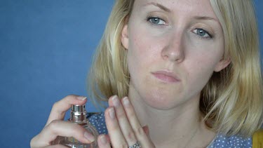 Young lady sprays perfumes on her hand first and than applies it to her neck.