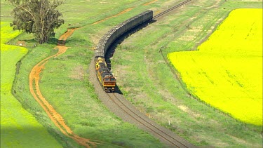 Goods train railway, windmill and canola field, Manildra.  Also called rapeseed; oil seed rape or rapaseed. Concept: sustainability, transport, environment, climate change, global warming, resources,...