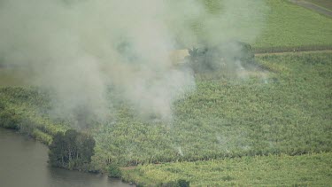 Smoke, fire agricultural land. Could be crop burning of sugarcane. River