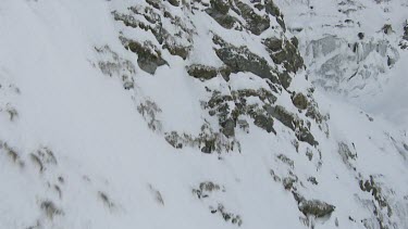 Waterfall or thawing snow water runs down steep cliff on snowy mountains.