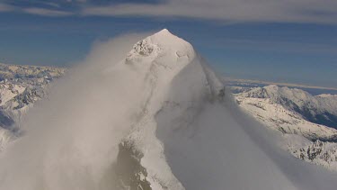 Wind blows strongly covering mountain peak summit in cloud. Shot shows cloud, mist travelling up the mountain. The clouds are brightly illuminated by the sunshine behind. Shows how wild weather can oc...