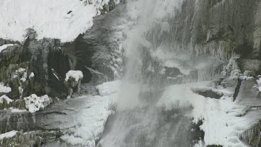 Waterfall crashing down steep slope of cliff face, could be caused by snow melt or a river