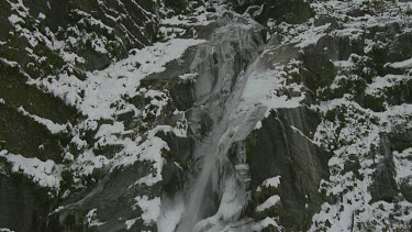 Waterfall crashing down steep slope of cliff face, could be caused by snow melt or a river