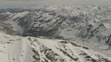 Wide shot snow covered peaks of mountain ranges , jagged rocky peaks and valley