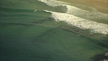 Aerial Bondi Beach, zoom out from people swimming, surfing,  in sea to wide shot of beach and suburbs across to city and harbour in background