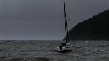Boat, yacht with sails down, out at sea with very rough stormy water. Boat tethered or anchored in shallow waters.