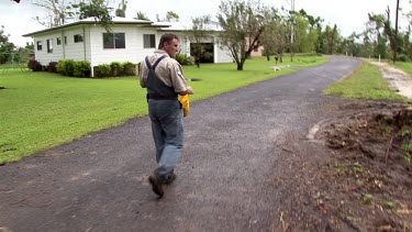 Park ranger walking along street carrying bag of fruit to try to attract cassowary to remove it from urban area.