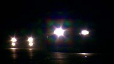 Approaching headlights of cars driving at night. White lights driving towards camera.