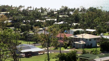 High-angle establishing shot of Mission Beach, small town in tropical north Queensland. Sparkling ocean in background, palm trees, houses with colorbond steel roofs.