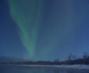 Timelapse of Aurora borealis. The Northern lights. Arctic circle. Green light dances over a lake and snow covered mountains.
