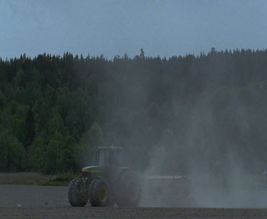 Agriculture farming, ploughing up land with tractor, dust lifts into air.
