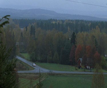 Car drives rural forested Scandinavian landscape. Farmhouse