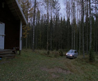 Car drives rural forested Scandinavian landscape. Farmhouse