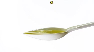 Olive Falling into Spoon with Olive Oil against White Background, Slow Motion
