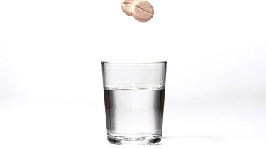 Tablets Falling and Dissolving into a Glass of Water against White Background, Slow Motion