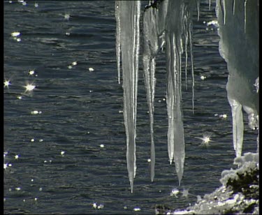 Sunlight glistens on sea surface, icicles hang down in foreground