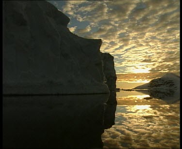 Track around iceberg. Clouds reflecting in still sea.