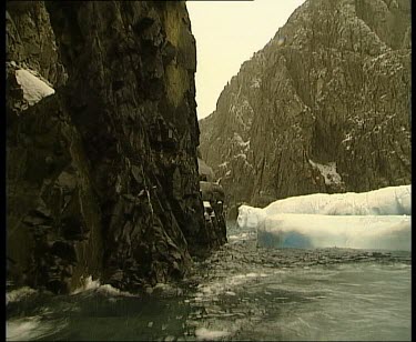 Fjord or sound. Long narrow coastal inlet between tall cliffs. Chunks of ice floating in sea.