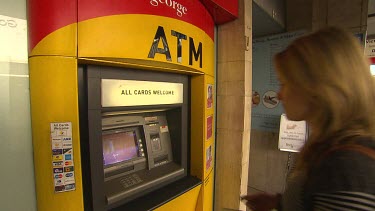 Bank automatic teller machine. ATM woman walks into shot to draw money. Close up, inserting card into cash machine. Inserting numbers and touching touch screen, removing cash from machine.