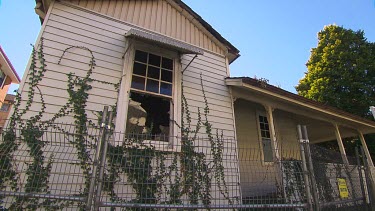 Derelict shingled wooden house with broken glass window. It has been condemned.