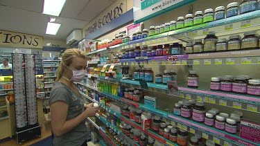 Woman wearing medical face mask looking at off the shelf pharmaceuticals, medicines, in pharmacy.