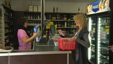Woman working at cash register in supermarket or small food shop serves customer