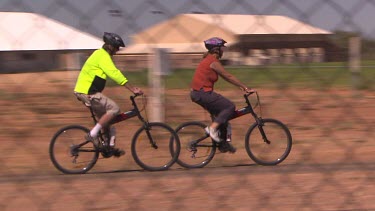Two people, woman and man riding bicycles ride past Birdsville bakery