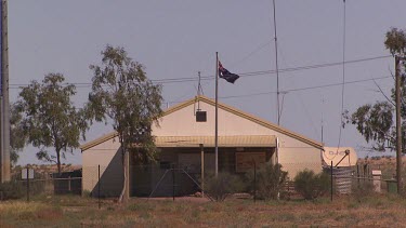 Building in Birdsville with corrugated iron roof and Australian flag. Satellite on RHS. Eucalyptus gum trees. Corrugated steel water tank.
